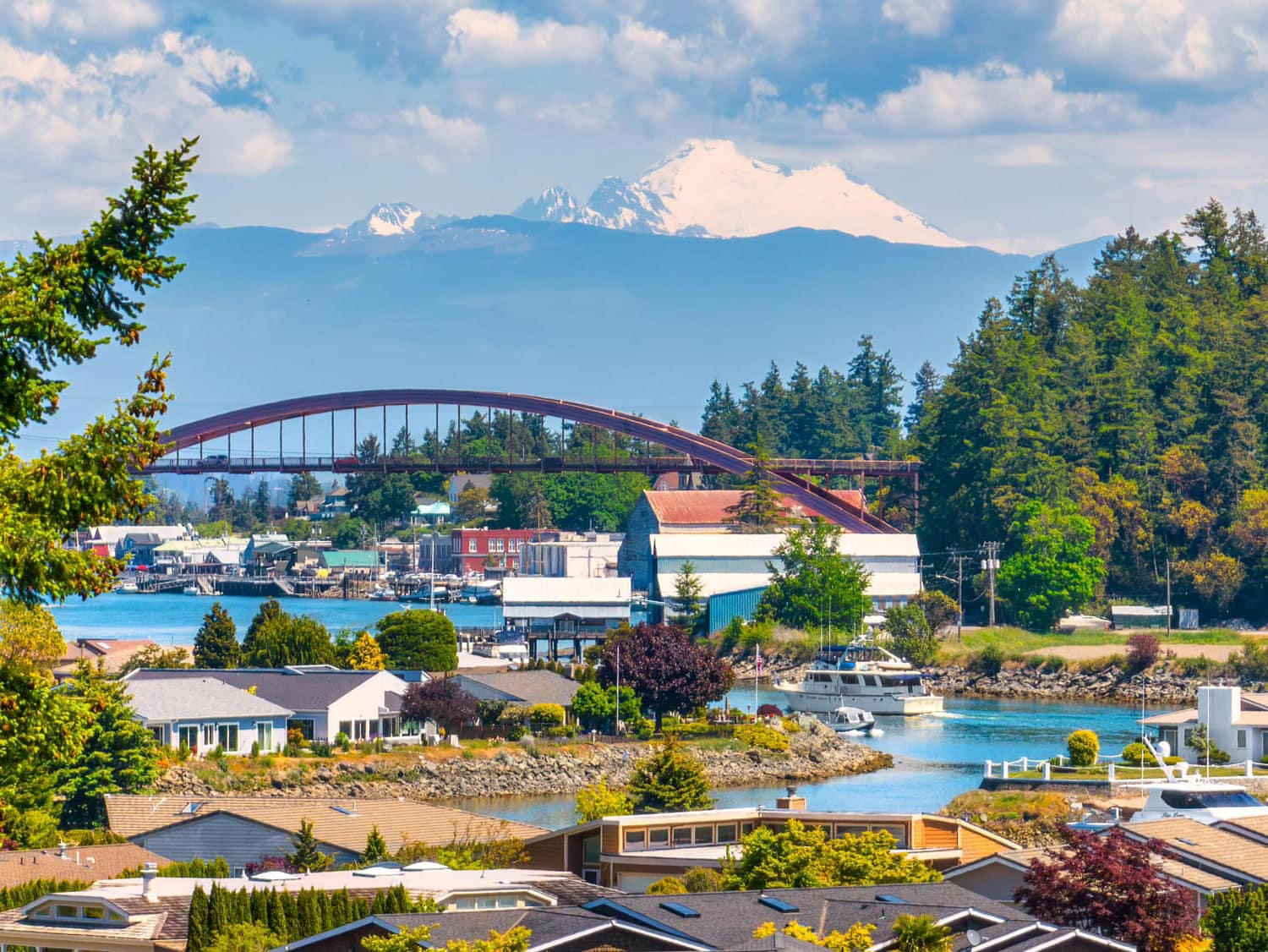 Aerial view of La Conner, Washington, featuring the Rainbow Bridge spanning the Swinomish Channel, with snow-capped Mount Baker rising in the background.