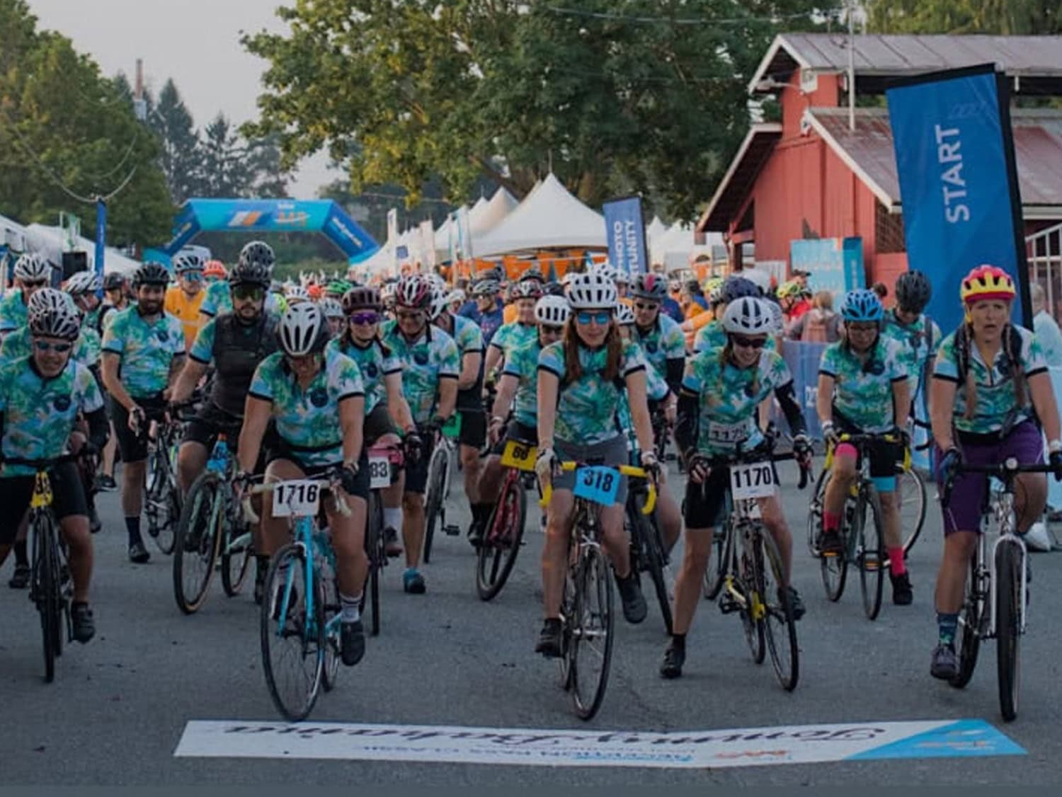 A large group of cyclists in matching jerseys launches from the start line at a community bike ride event in Skagit County, Washington