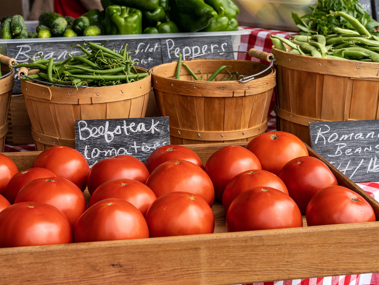 Fresh beefsteak tomatoes, romano beans, green beans, and peppers displayed in wooden baskets and crates at a Skagit Valley farmers market.